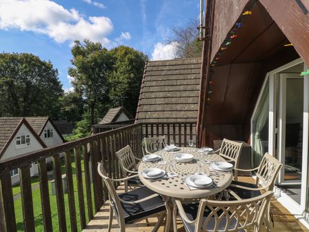 An outdoor balcony with a dining table set for six and surrounded by chairs at Devine Lodge in Callington