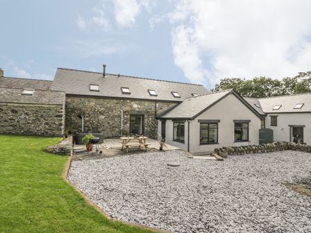 A stone and white exterior of a house with a gravel yard grass lawn and a picnic table at Storws in Pentraeth