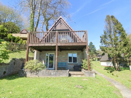 A wooden cabin with a balcony and garden surrounded by trees at Valley Lodge 44 in Callington