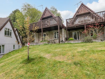 Two chalet style houses with wooden balconies and a grassy lawn with small trees at Valley Lodge 5 in Callington