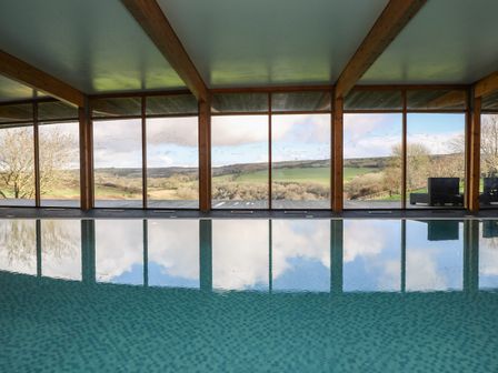 An indoor pool with large windows showing a countryside view at Westhayes in Camelford