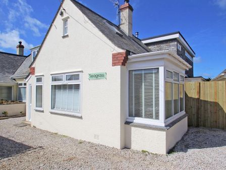 A cream house with multiple windows and a sign saying Seagrass on the wall with a gravel driveway at Seagrass in Crantock Nr Newquay