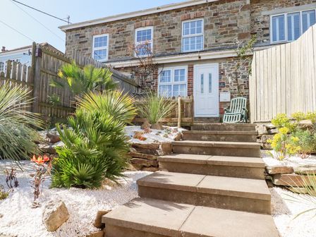 Stone house with white door and windows with steps leading to garden with palm plants and white gravel at Alma House 2 in Perranporth