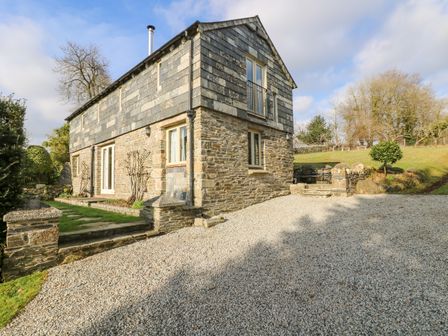 A stone house with gravel driveway and grass areas surrounded by trees at Woodfield Coach House in Merrymeet