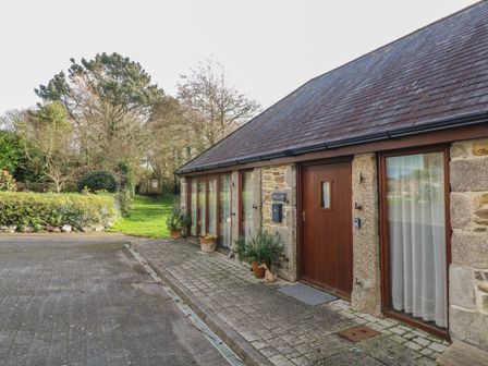 A stone cottage with wooden doors and windows next to a paved area and a grassy path at Willow in Falmouth