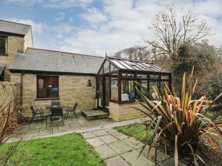 A stone house with a glass conservatory and outdoor seating area at Chy-Nans in Falmouth