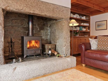 A living room with a wood burning stove in a stone fireplace a red leather sofa and wooden shelves at Halvosso in Falmouth