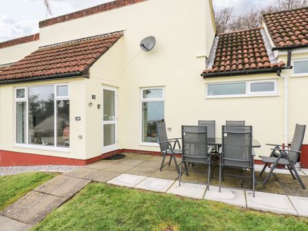 A patio with outdoor table and six chairs beside a house with tiled roof and large windows at Manorcombe 19 in Callington