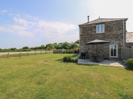 A stone house with a patio area that has a table, chairs, and umbrella on a grassy lawn at Sundowner in Padstow