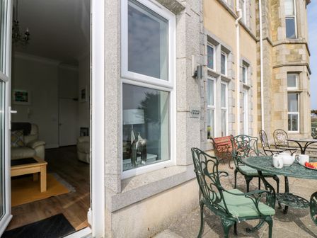 An outdoor patio with metal chairs and a table with teapot and cups outside a stone building at By The Sea in Newquay