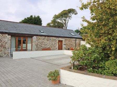 An outdoor area with stone-paved ground plants in pots and a stone building with wooden doors and windows at Hazel Barn in Falmouth