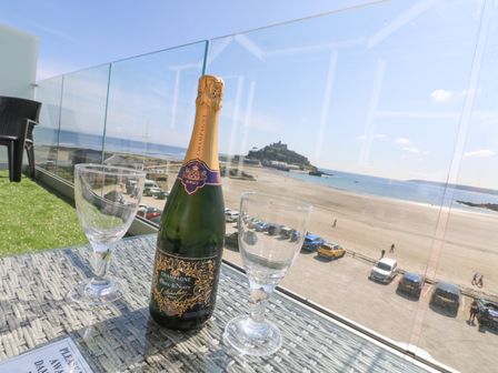 A bottle of champagne and two glasses on a table on a balcony overlooking a beach and a castle on a hill at Higher Mount View in Marazion