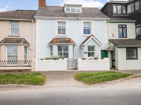 A blue house with white trim and a small garden behind a white wall and gate at Cool Stone Cottage Instow near Bideford