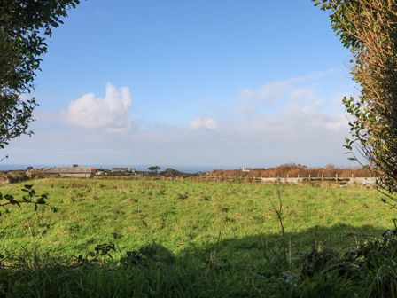 A grassy field with a few buildings and trees in the distance under a blue sky with clouds at Five Degrees West in St Just