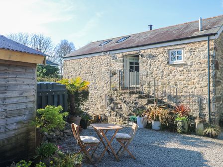 An outdoor stone patio with wooden table and chairs and potted plants near stone building at Trevoole Barn in Praze An Beeble