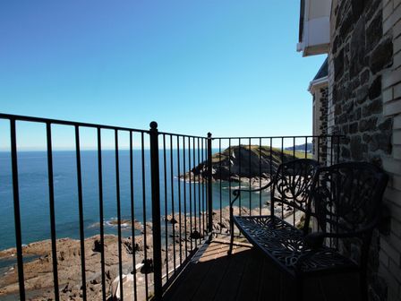 A balcony with metal bench and railing overlooking the sea and rocky coastline at Ocean Breeze in Ilfracombe