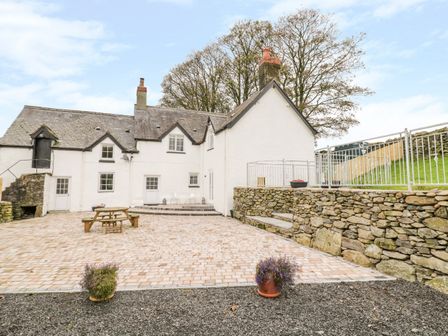 An outdoor courtyard with a wooden picnic table and stone walls around a white house at Tai Ucha in Cerrigydrudion