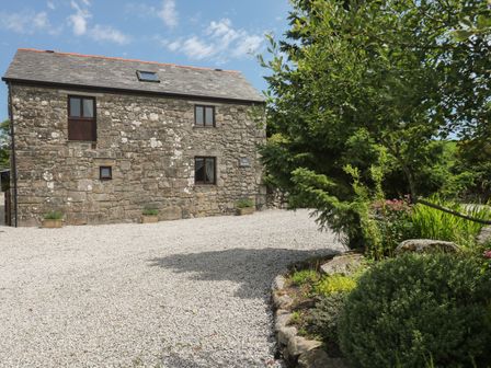 A stone building with three windows and a gravel driveway with plants and trees on the side at The Hayloft in St Neot near Dobwalls