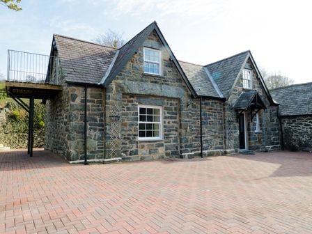 An exterior view of a stone house with slate roof and a brick paved driveway at The Coach House in Llanrwst