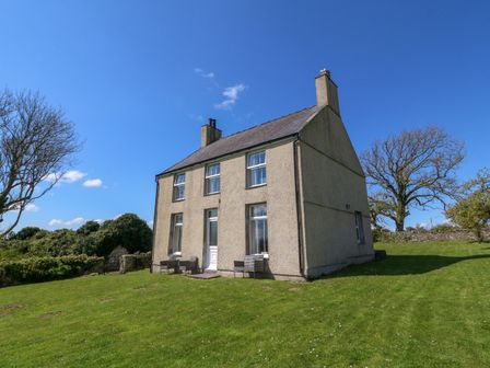 A two-story house with outdoor chairs on a lawn with trees at Ty Mawr in Llanddaniel Fab