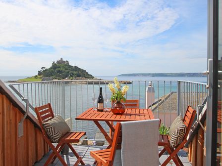 A balcony with a wooden table and chairs overlooking the sea and a castle on an island at Star House in Marazion