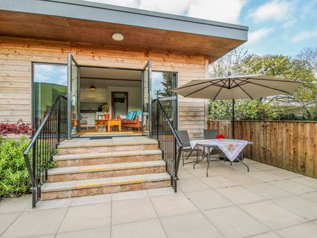A patio with table chairs and umbrella next to steps leading to a room with open glass doors at No1 The Lodge Acton near Bishops Castle