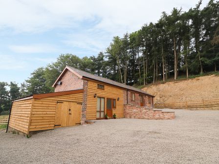 A brick and wooden house with a gravel driveway and trees on a hill at Pentre Fach in Llandrindod Wells