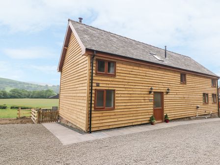 Exterior view of a wooden house with a gabled roof and multiple windows surrounded by gravel and a grassy field at Pentre Fawr in Llandrindod Wells