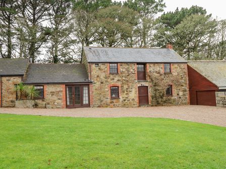 A stone cottage with wooden doors and windows surrounded by trees and a grassy lawn at Barn Cottage Marazion