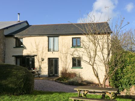 An exterior view of a two story stone house with a garden and picnic benches at Carthorse Cottage in Teignmouth