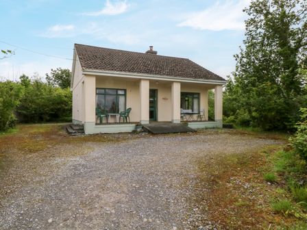 A single story house with a tiled roof and a gravel driveway surrounded by trees at Hideaway in Cahir near Ballinrobe County Mayo