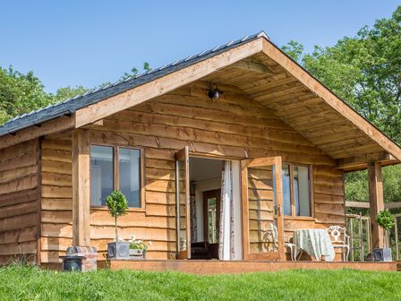 A wooden cabin with open doors and windows a table with chairs outside on a porch at Stoney-Brook Lodge in Bedlam near Ludlow