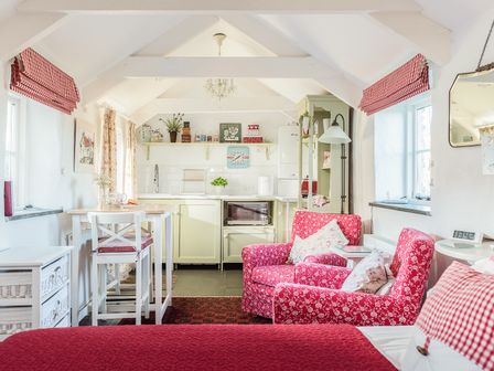 A small kitchen and living area with red patterned chairs and checkered curtains at The Snug in Rescorla near St Austell