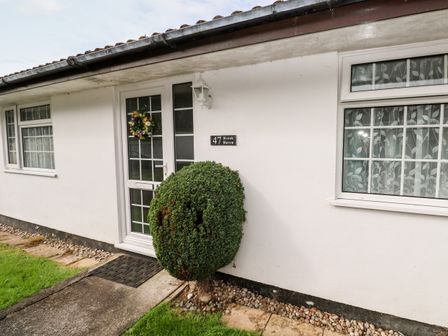Front entrance of a white house with a trimmed round bush near the door and windows at Brook Haven Rosecraddoc Lodge near Liskeard Cornwall