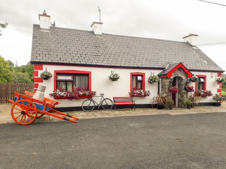 A cottage with flowers in window boxes a bicycle a bench and a cart on a paved area at Cookies Cottage in Ballyshannon County Donegal