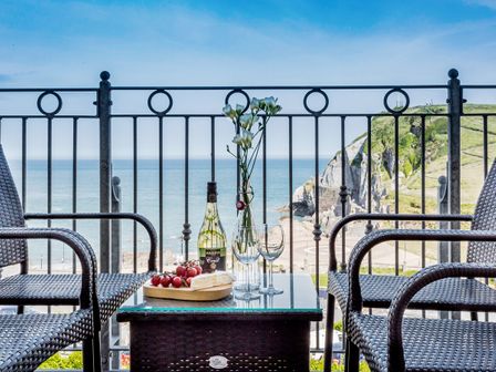 A balcony with two wicker chairs and a table with wine glasses grapes and flowers overlooking the sea at No 6 Arlington Villas in Ilfracombe