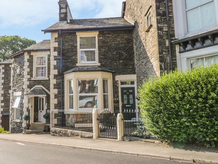 A stone house with a bay window and a gated front garden on a street at Ivy Bank in Windermere