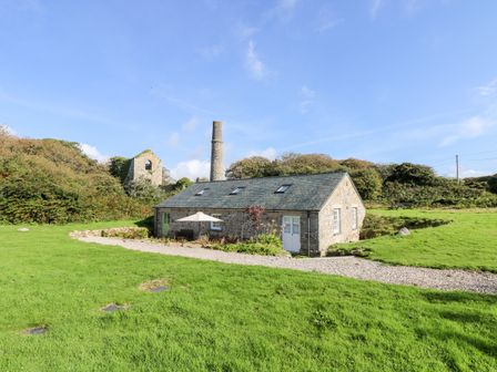 A stone cottage with a slate roof surrounded by grass and bushes at Wheal Grey in Praa Sands