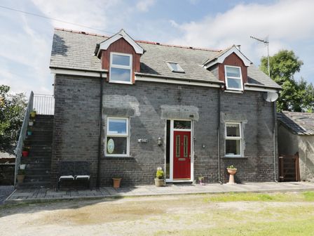 A two story brick house with a red front door and exterior stairs on the left at Hen Stabl in Llanrwst