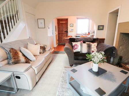 A living room with two sofas a coffee table with flowers and an archway to a kitchen at Corbett Cottage in New Haggerston near Holy Island