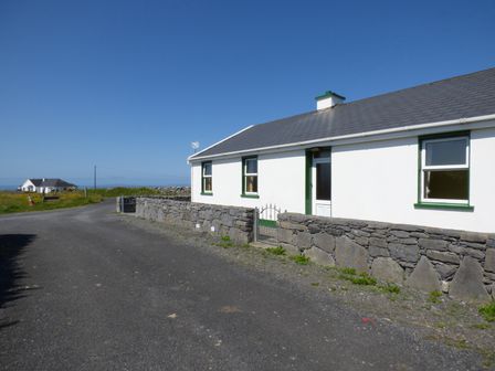 A white cottage with green window frames and a stone wall along a country road at Seaview Cottage in Fanore County Clare