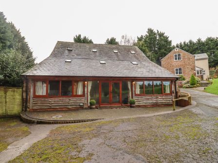 A front view of a house with a slate roof and wooden framed windows surrounded by trees at The Old Stables in Upton Bishop near Ross-on-Wye