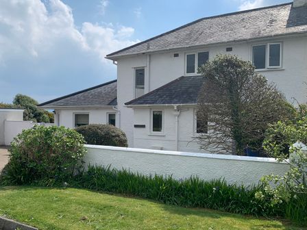 The exterior of a white house with a slate roof and bushes along a white wall at The Beach House Criccieth
