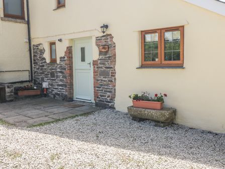The exterior of a cottage with a pale green door stone wall accents two windows and flower pots on stone benches at Lower West Curry Cottage in Launceston