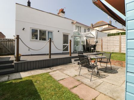 A backyard with a raised wooden deck and a patio area with metal chairs and a glass table at Pier View in Paighton