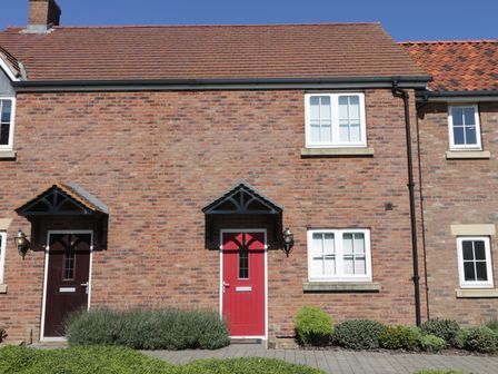 Front of a brick house with a red door and adjacent brown door with small porches and windows at 104 Sunrise Drive in Filey
