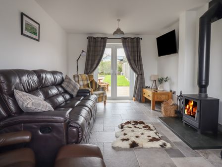 A living room with a leather sofa armchair wood burning stove and glass doors leading to a garden at Gwynfa in Rhyd Uchaf near Bala Gwynedd