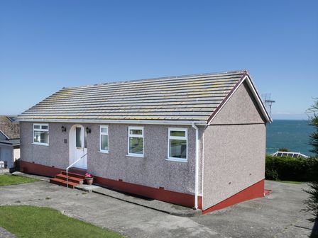 A single-story house with a tiled roof and white door overlooking the sea at Bay Lodge in Bull Bay