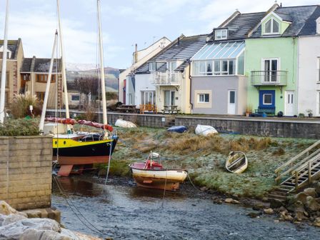 Boats tied up near a stone wall by a row of houses with a small river and grassy bank at Harbourside House in Haverigg near Millom