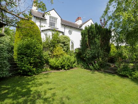 A garden with green grass and bushes in front of a white house with multiple windows at Bron Y Graig in Conwy